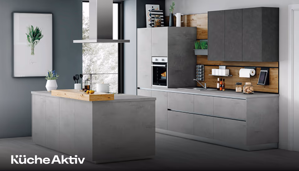 Moderne Küche in grauer Betonoptik mit Insel, Hängeschränken und Holzrückwand, ausgestattet mit Backofen, Dunstabzugshaube und dekorativen Accessoires vor großem Fenster